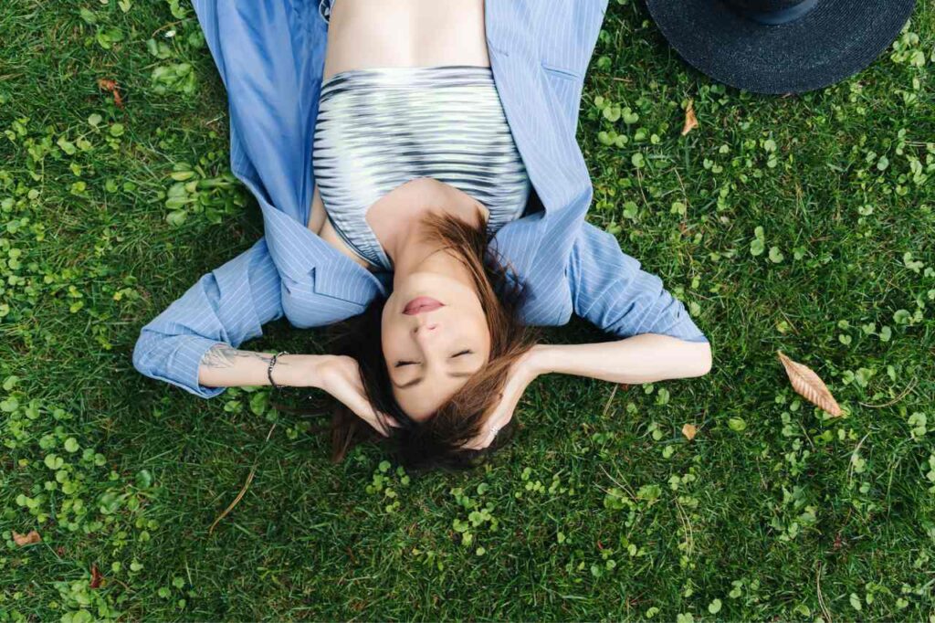 A young Caucasian woman lays on the grass, looking happy.