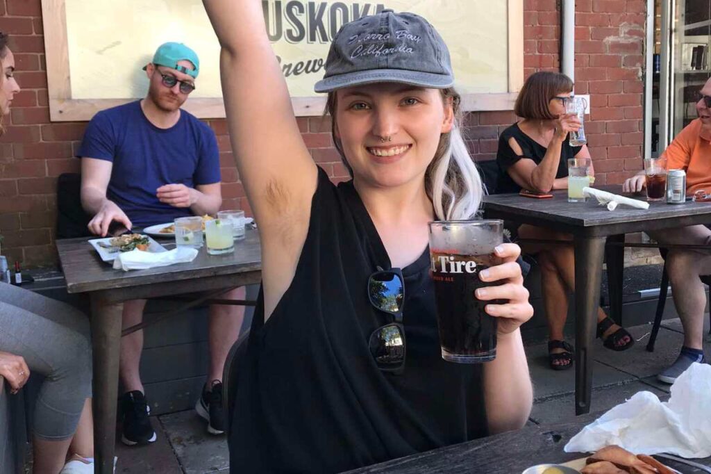 Madison holding a drink and eating food outdoors at a public restaurant.