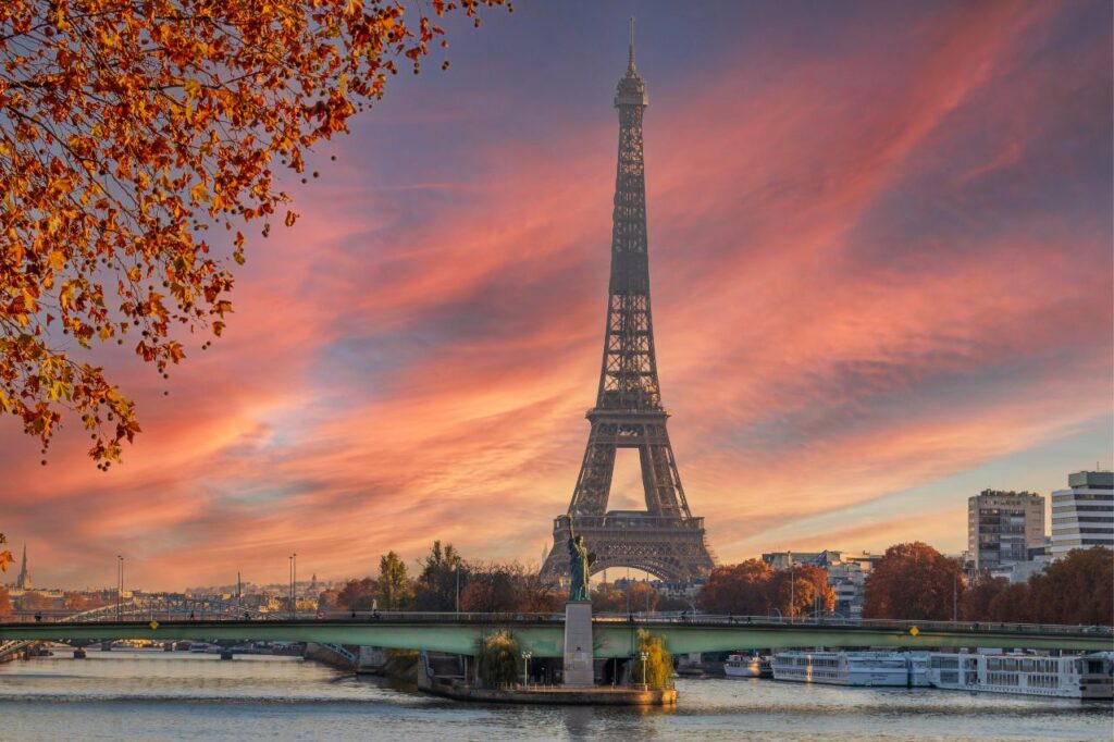 The Eiffel Tower in Paris during the fall stands in front of a beautiful pink sunset.