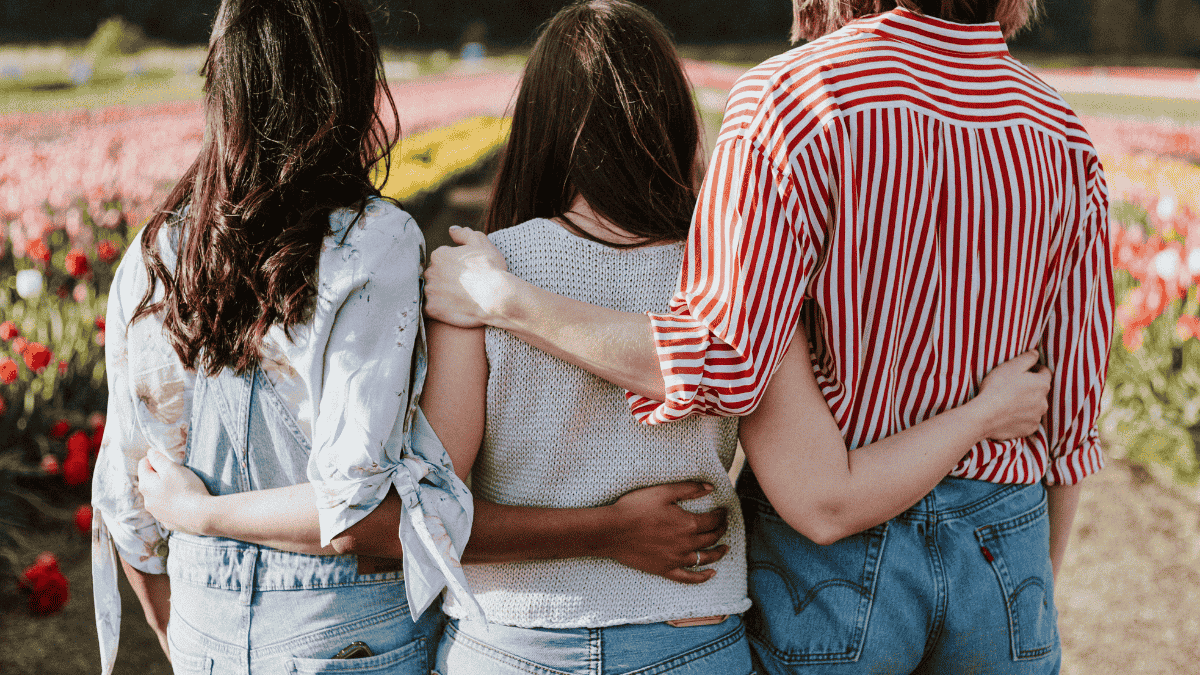 Three women standing with their arms wrapped around one another, facing away